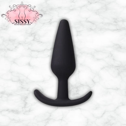 Plug anal en silicone noir de forme conique vendu par Sissy Transformation Shop sur fond marbre
